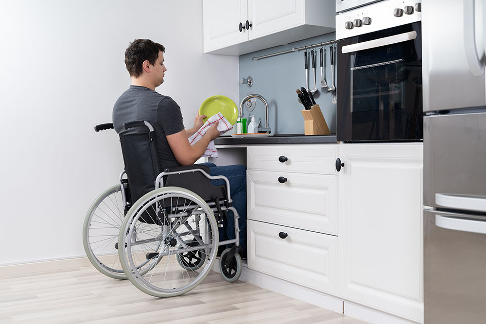 Persoon in rolstoel in een aangepaste keuken die de afwas doet.