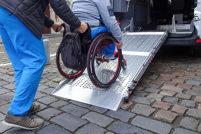 Persoon die andere persoon in rolstoel via plank in auto begeleid.